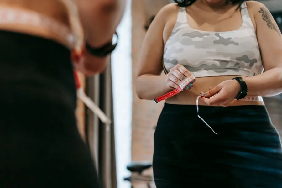 Woman measuring her waist with a tape measure to track weight loss progress